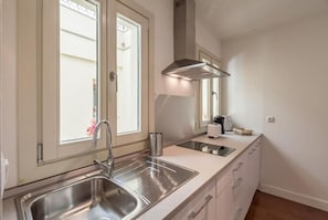 Una cocina moderna con un lavaplatos de acero inoxidable, una ventana con persianas, una estufa empotrada y una campana extractora.