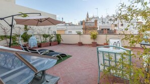 A rooftop terrace with potted plants, a glass table, and a metal chair. - Roof Cathedral Sevilla (Sevilla)