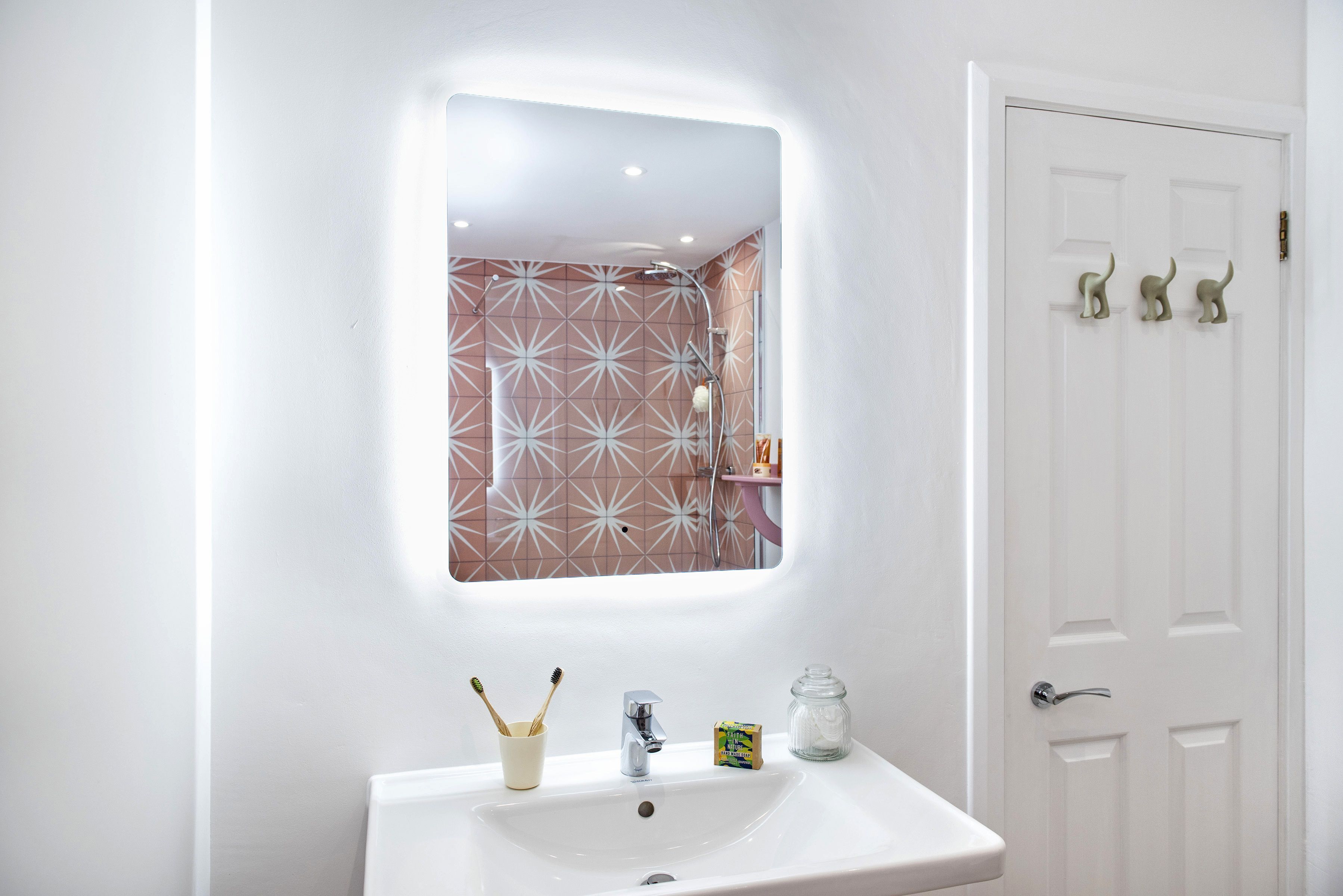 A bathroom with a white sink, a mirror, and a door with dinosaur-shaped handles.