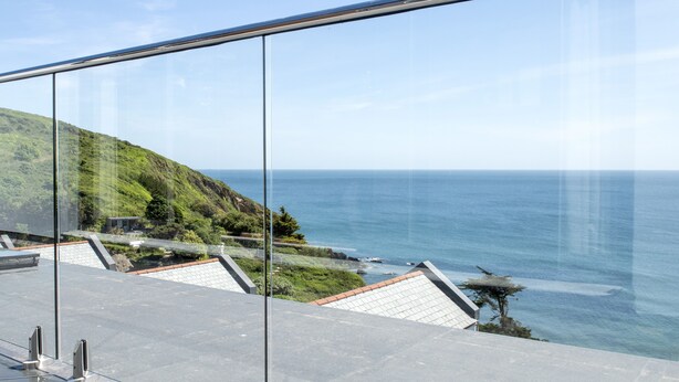 Een modern gebouw met een glazen balkon dat uitkijkt over een kustlandschap.