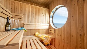 Een houten sauna met een bank, een tafel met fles en glazen, en een raam met uitzicht.