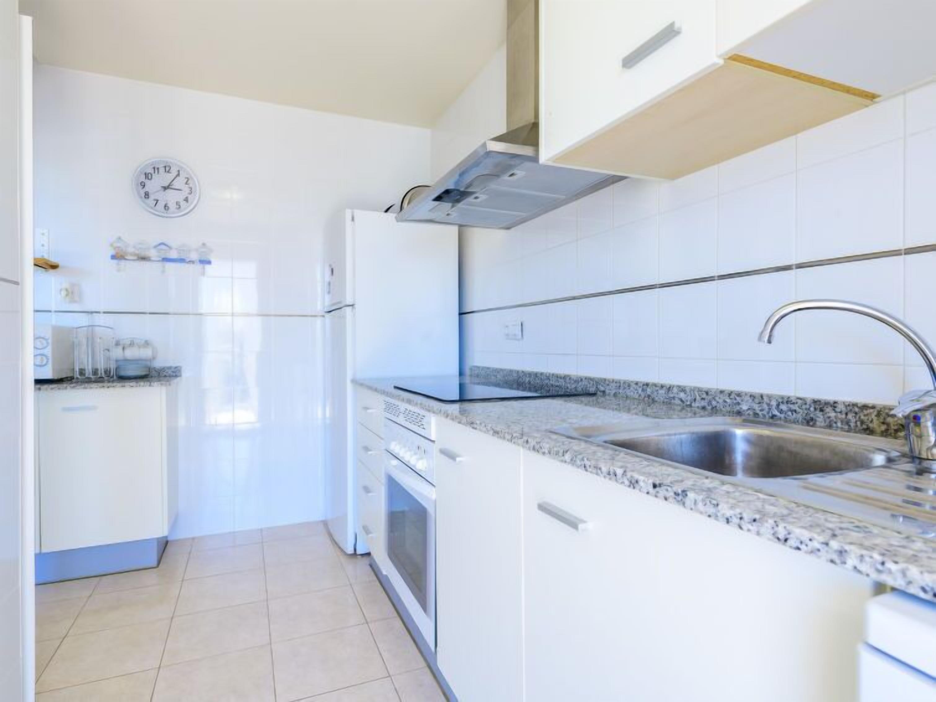 Een moderne keuken met witte kasten, een roestvrijstalen spoelbak en een klok aan de muur.