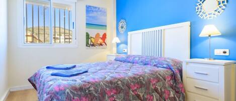 Un dormitorio con cama, mesita de noche, lámpara, ventana con vistas y decoración en la pared.
