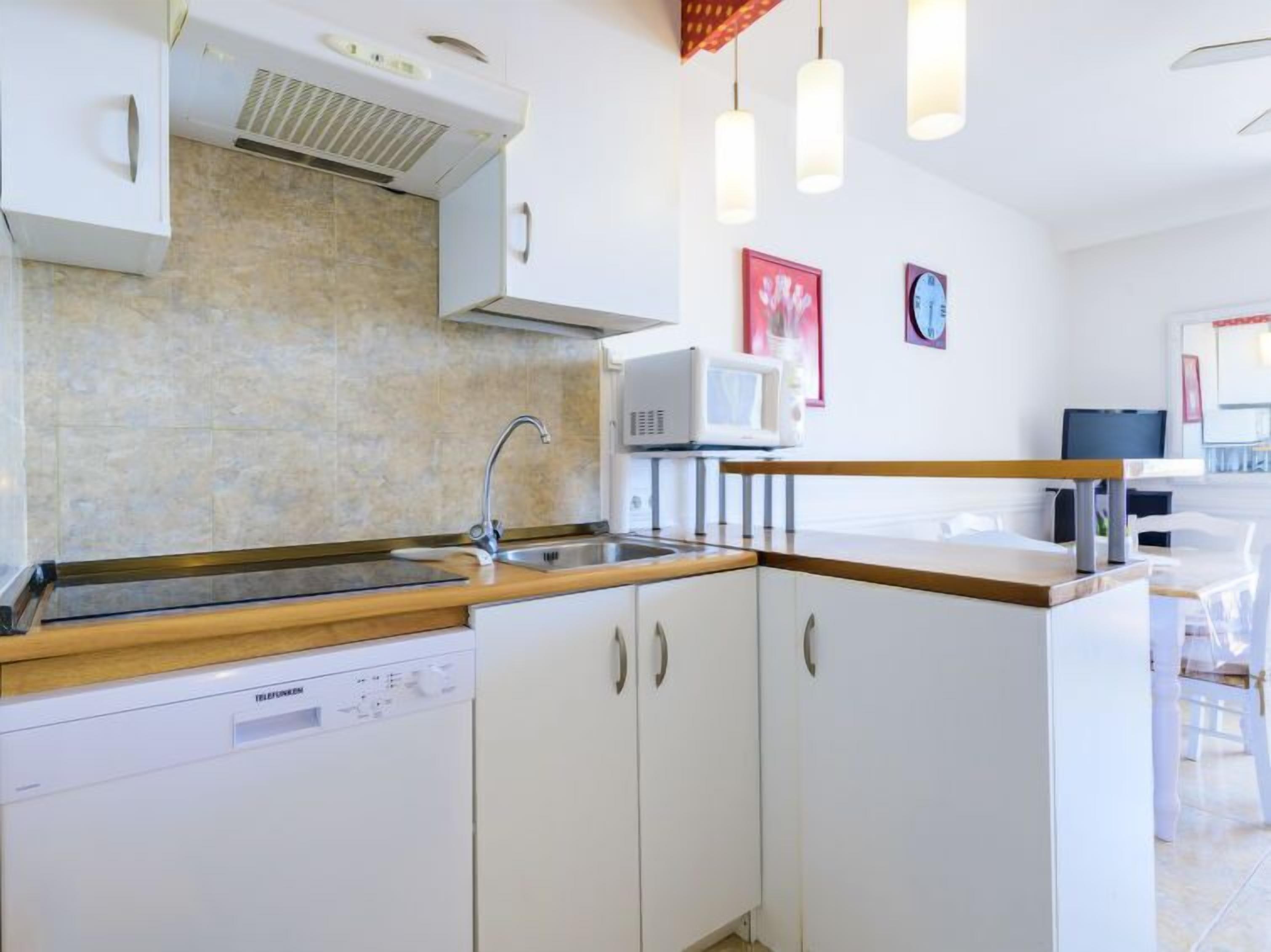 Eine moderne Küche mit weißen Schränken, einem Geschirrspüler, einer Mikrowelle und einer Holz Arbeitsplatte.