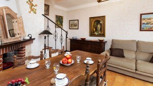 A dining area with a wooden table set for four, surrounded by chairs. There is a fireplace with a brick mantle, a chandelier, and artwork on the walls. - Apartment Cathy by Interhome (Llançà)