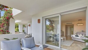 A modern outdoor seating area with white furniture and a glass door leading to an interior living space. - Altos de la Quinta by Interhome (Marbella)