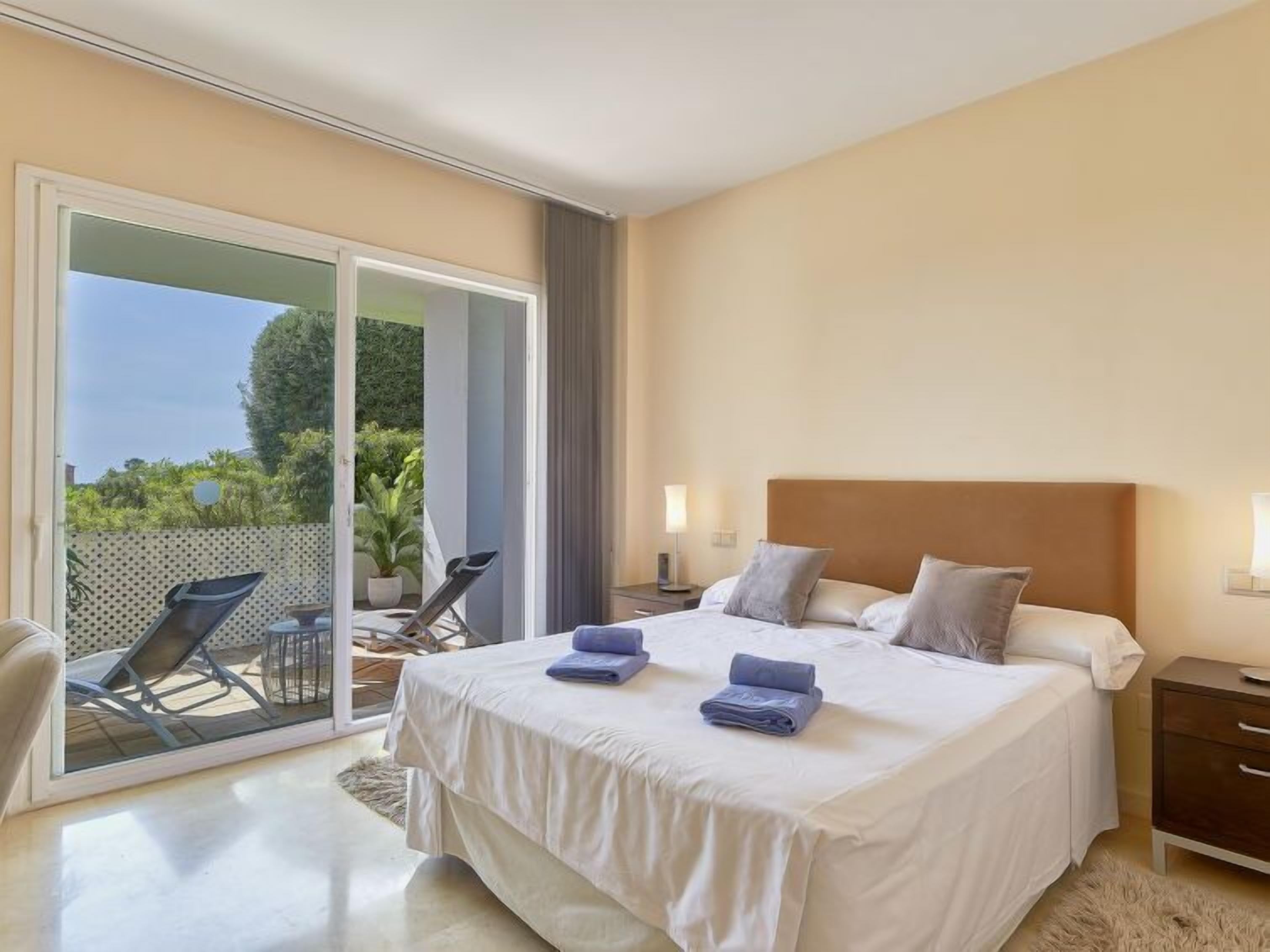 Un dormitorio con una cama grande, una mesita de noche, una silla y vistas al exterior.