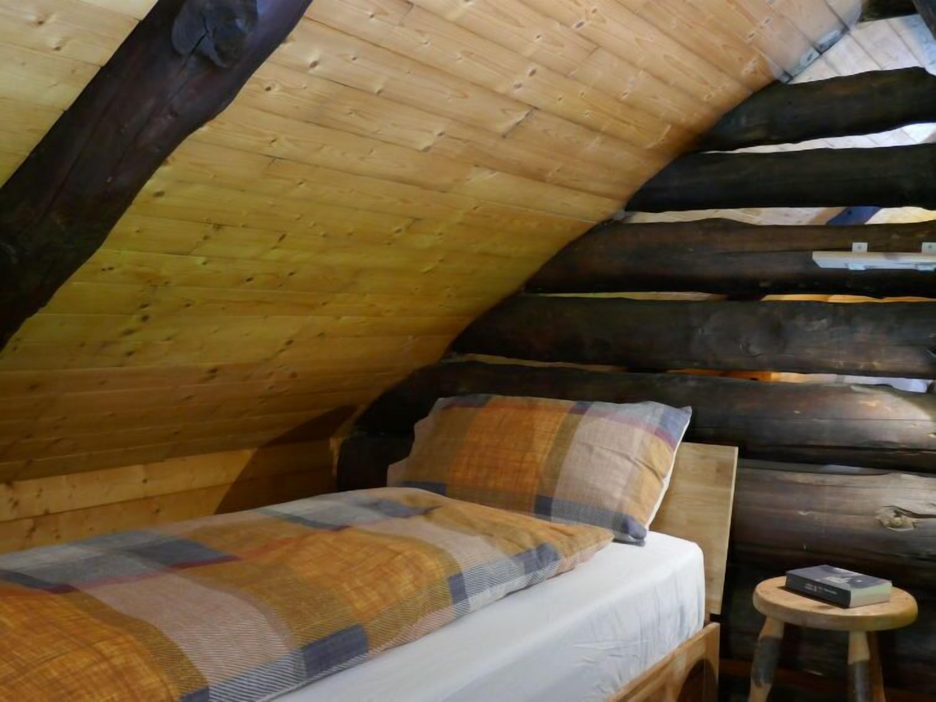 A cozy log cabin bedroom with a bed, pillows, and a small stool with a book.