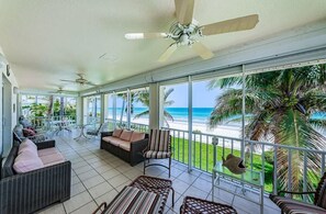 A covered outdoor area with wicker furniture, ceiling fans, and a view of the beach.