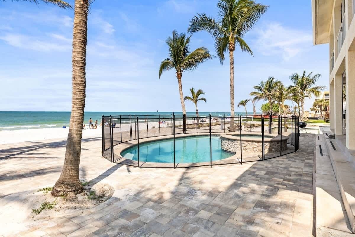 A pool surrounded by palm trees, a beach, and a building.