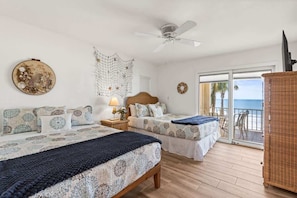 A hotel room with two beds, a ceiling fan, a balcony with a view, and a wicker cabinet.