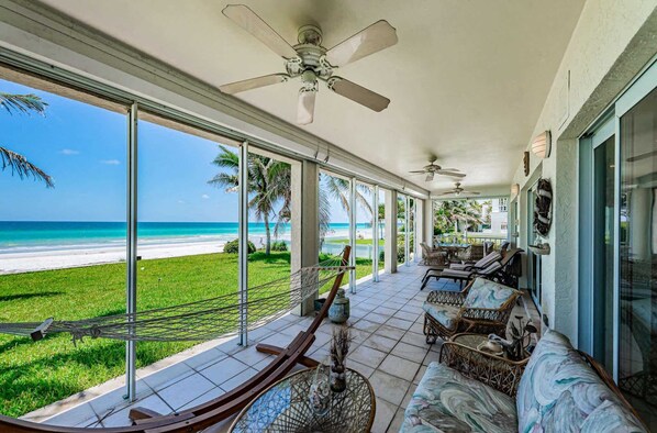 A covered outdoor area with a view of the beach, seating, and ceiling fans.