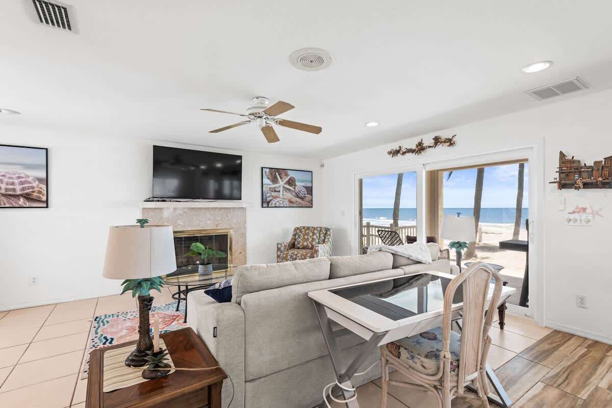 Ein Wohnzimmer mit einer Couch, einem Fernseher, einem Deckenventilator und Blick auf den Strand.