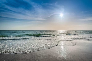 A beach with waves, a clear sky, and the sun.