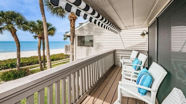 A balcony with white wicker furniture, a view of the beach, and palm trees. - Aldea 14 Beachfront Townhouse in Belleair Beach (Belleair Beach)