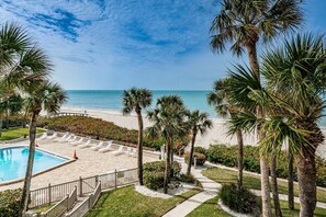 A pool area with lounge chairs, palm trees, and a view of the beach.