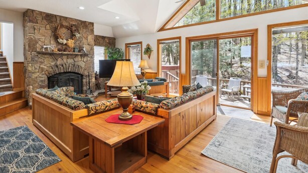 A cozy living room with a stone fireplace, a wooden bench, and a large window overlooking a forest. - Cedar Dome: 3  BR, 3  BA House in Canaan Valley, Sleeps 8 (Canaan Valley)