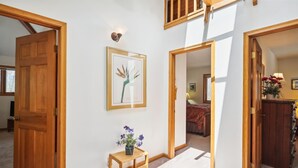 A hallway with wooden doors, a framed artwork, a small wooden table with a vase of flowers, and a view into a bedroom with a bed and a lamp. - Cedar Dome: 3  BR, 3  BA House in Canaan Valley, Sleeps 8 (Canaan Valley)