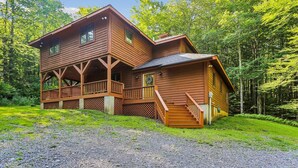 A two-story log cabin with a porch and a covered porch area, surrounded by lush greenery. - Cedar Dome: 3  BR, 3  BA House in Canaan Valley, Sleeps 8 (Canaan Valley)