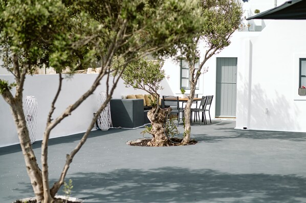 Un patio moderno al aire libre con una mesa de comedor y sillas, rodeado de paredes blancas y algunos árboles.