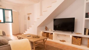 Ein modernes Wohnzimmer mit Couch, Fernseher auf weißem Schrank und Holztisch, sowie einer Treppe mit geneigter Decke.