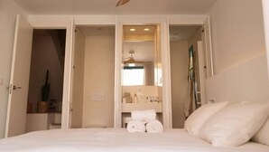 Ein Schlafzimmer mit Bett, Deckenventilator und einem durchgegangenen Türrahmen sichtbarem Badezimmer.