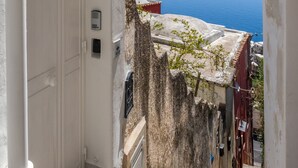 A narrow stairway leading to a white door with a small step, a metal bell, and a security device on the wall. - Blue Waves (Positano)