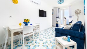 A modern living room with a white dining table, blue sofa, and patterned floor tiles. - Blue Waves (Positano)