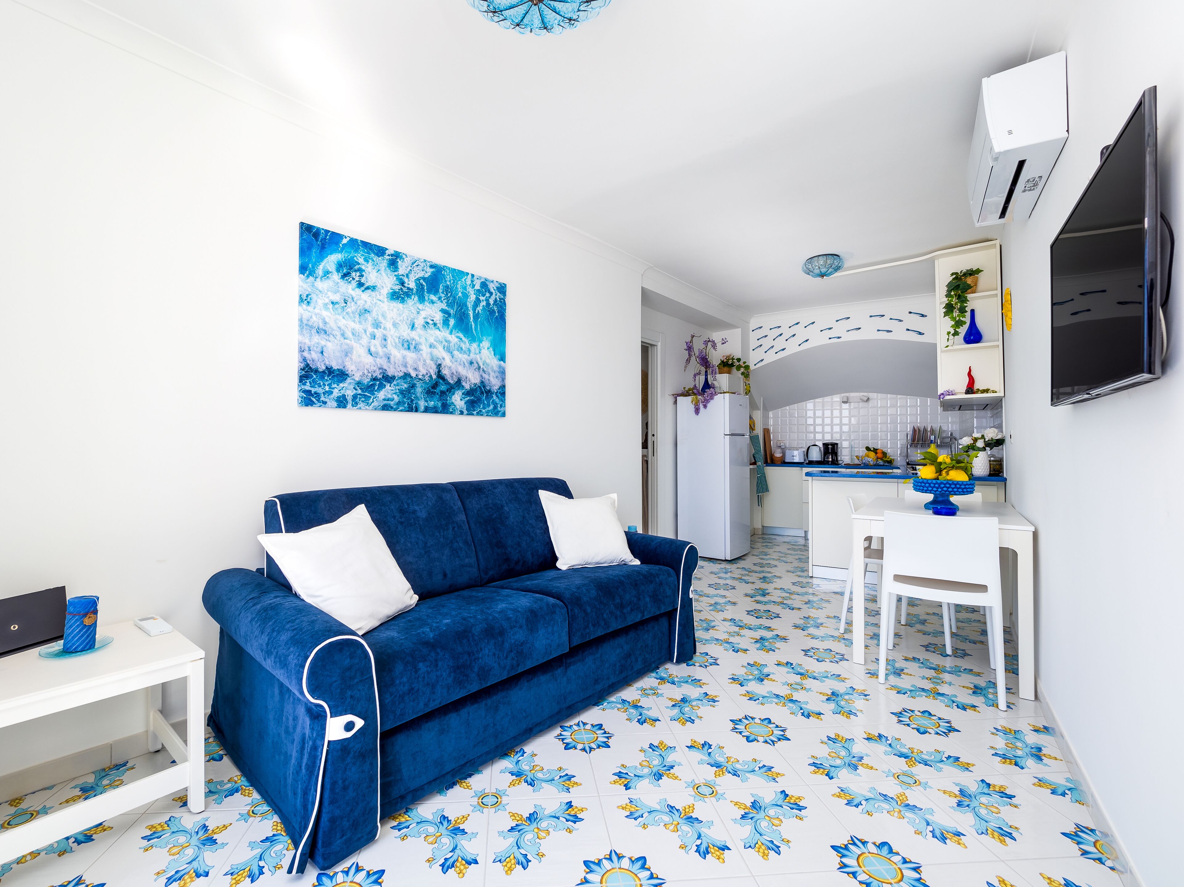 A modern living room with a blue sofa, a white table, and a kitchen in the background.