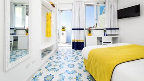 A hotel room with a bed, a TV, a bathroom with a mirror, and a balcony with a view. - Blue Waves (Positano)