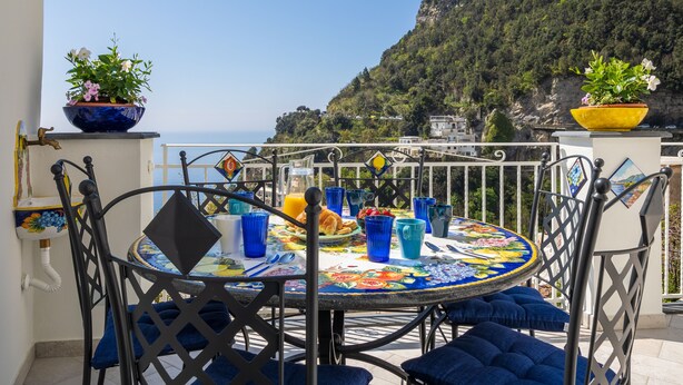 A round table with a colorful tablecloth, blue cushions, and a potted plant. - Blue Waves (Positano)