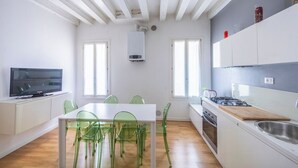 A modern kitchen with white cabinets, a gas stove, and a sink. There is a dining table with green chairs. - Rialto al Manganer (Venice)