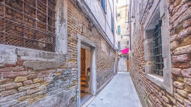 A narrow alleyway with stone walls and a metal gate, leading to a building with an open doorway. - Rialto al Manganer (Venice)