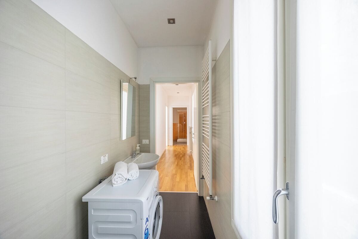 Un couloir étroit avec un lave-linge, un évier et un miroir sur le mur de gauche.