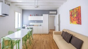 A modern kitchen with white cabinets, a dining table with green chairs, and a beige sofa. - Rialto al Manganer (Venice)