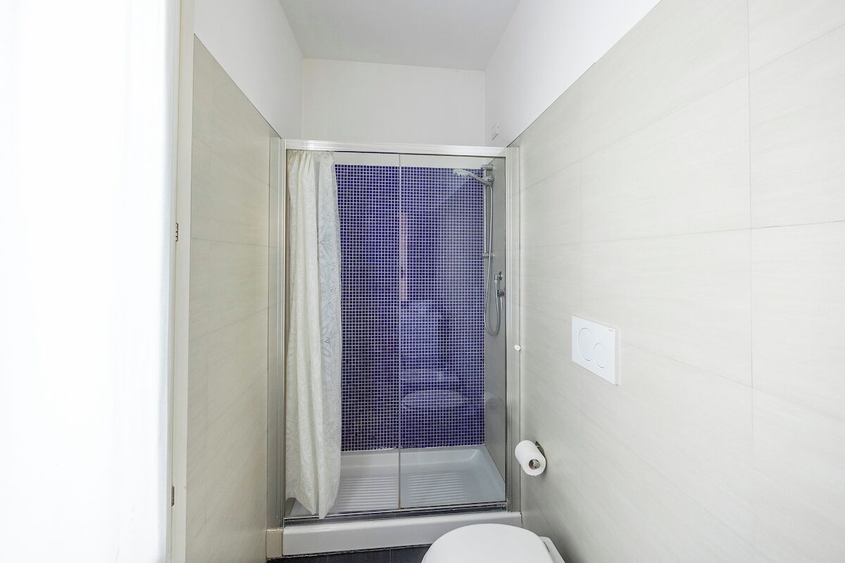 Un baño pequeño con ducha, azulejos blancos y un inodoro.