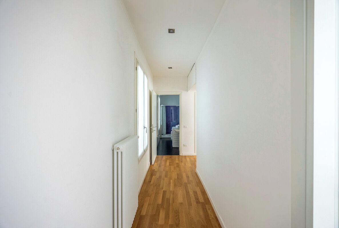 Un corridoio stretto con pavimento in legno e pareti bianche, che conduce a una stanza con una porta blu.