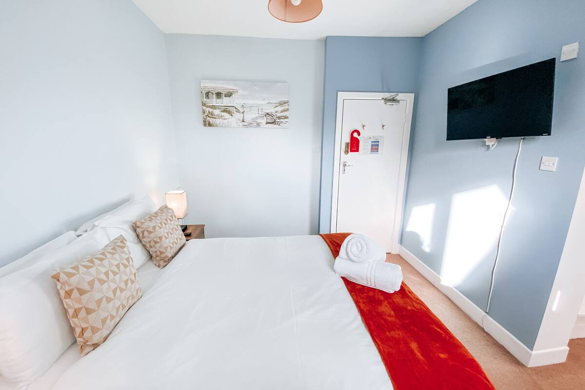 Ett hotellrum med en stor säng, en tv som är monterad på väggen och en dörr med ett rött handtag.