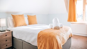 A neatly made bed with white and orange bedding, a bedside table with a lamp, and a window with curtains. - Ingledene Guest House  (Bournemouth)