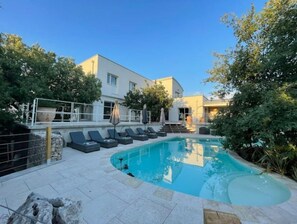 Et moderne poolområde med liggestole, en klar blå pool og en bygning med store vinduer.
