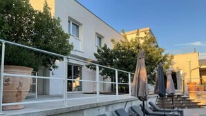 Ein Poolbereich mit Liegestühlen und Sonnenschirmen, ein weißes Gebäude mit Fenstern und ein Geländer.