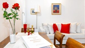 Un salon avec un canapé blanc, des coussins rouges, une table basse en bois et un tableau encadré au mur.