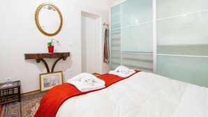 Une chambre d’hôtel avec un lit, une table de chevet dotée d’un miroir, un plaid rouge et un cadre photo.