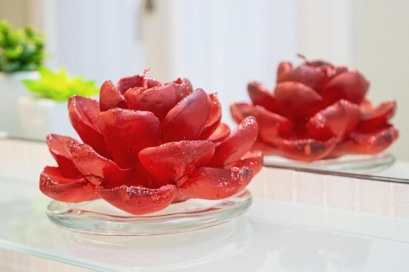 Un tazón de vidrio transparente con un objeto rojo, con forma de flor, sobre una superficie reflectante.