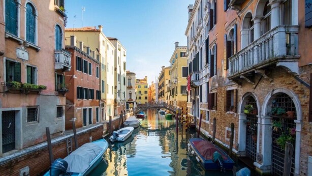 Un canal étroit à Venise, bordé de bateaux amarrés de part et d’autre.