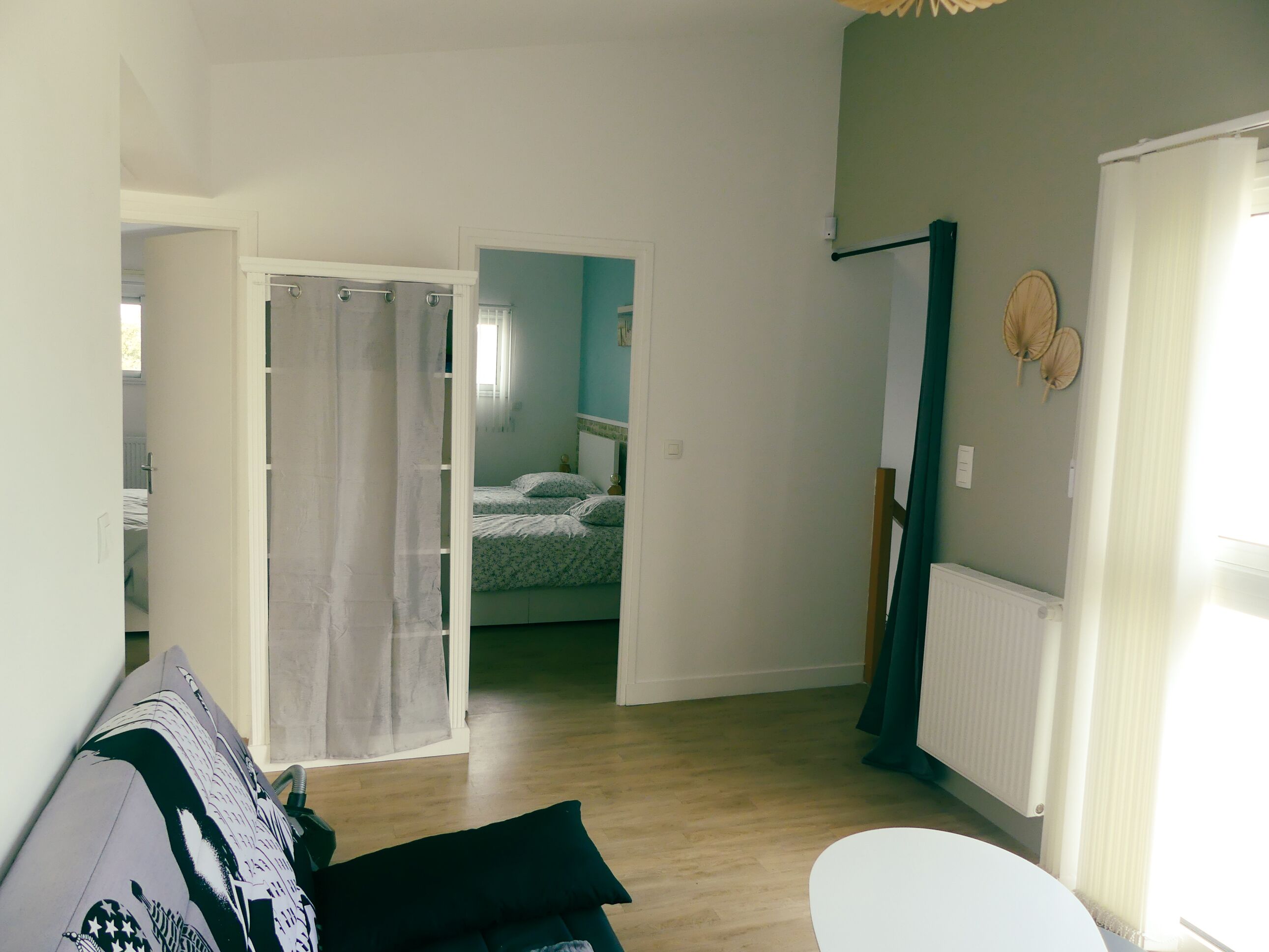 A room with a bed, a white chair, a sofa, and a bathroom visible through an open door.