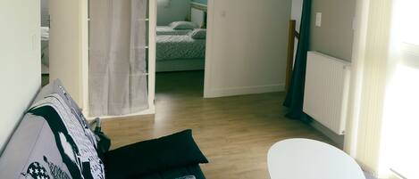 A room with a bed, a white chair, a sofa, and a bathroom visible through an open door.