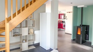 Una sala de estar moderna con una escalera de madera, un radiador blanco y una estufa de leña.