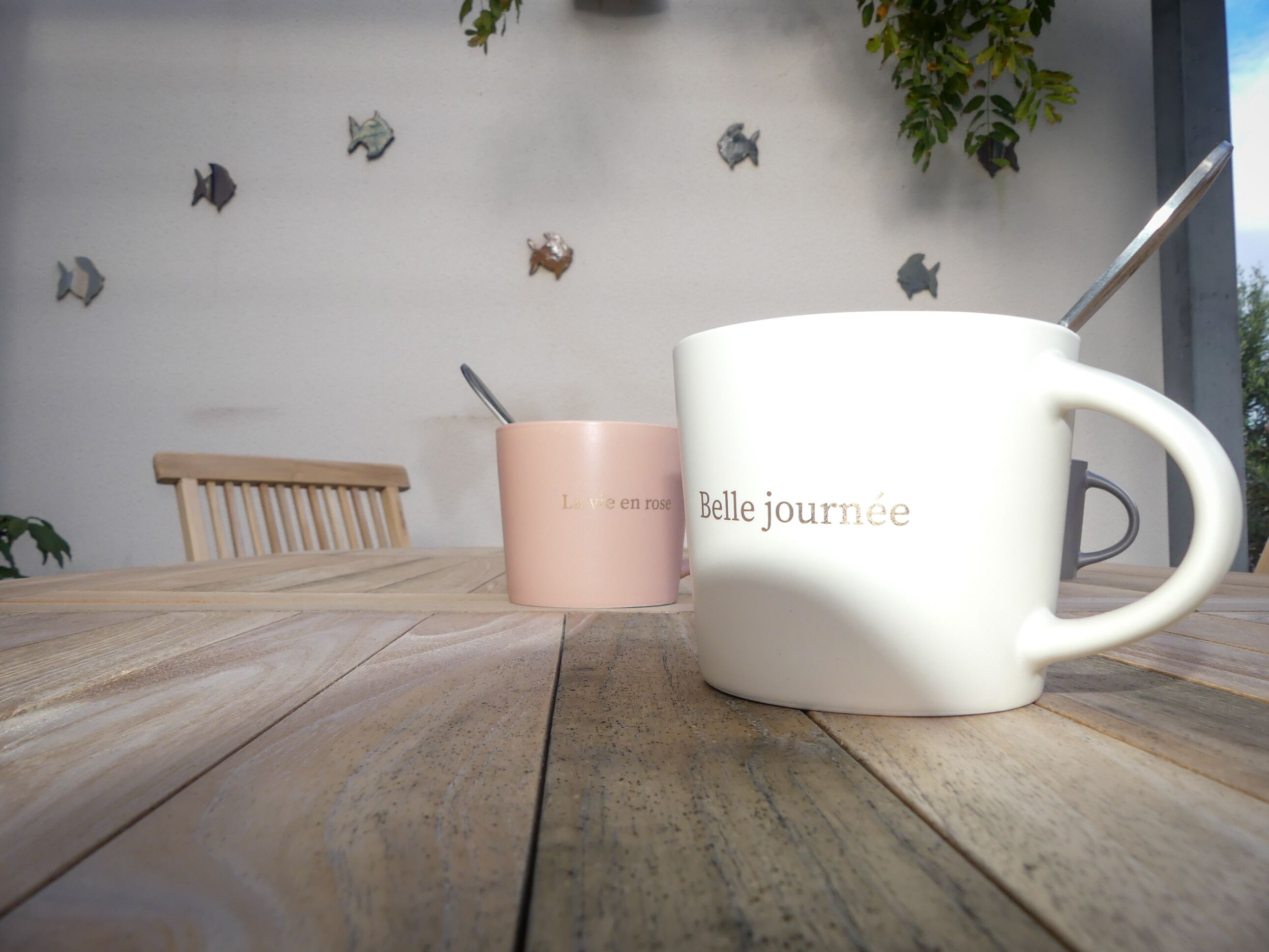 Une tasse blanche avec une cuillère, une tasse rose et un banc en bois sur une table en bois.