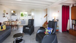 Een moderne woonkamer met een bank, twee fauteuils, een salontafel, en een eethoek met stoelen en een tafel.